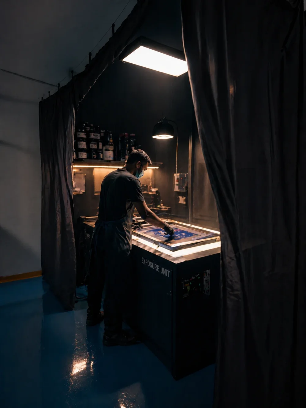 A technician preparing a printing screen on an exposure unit
