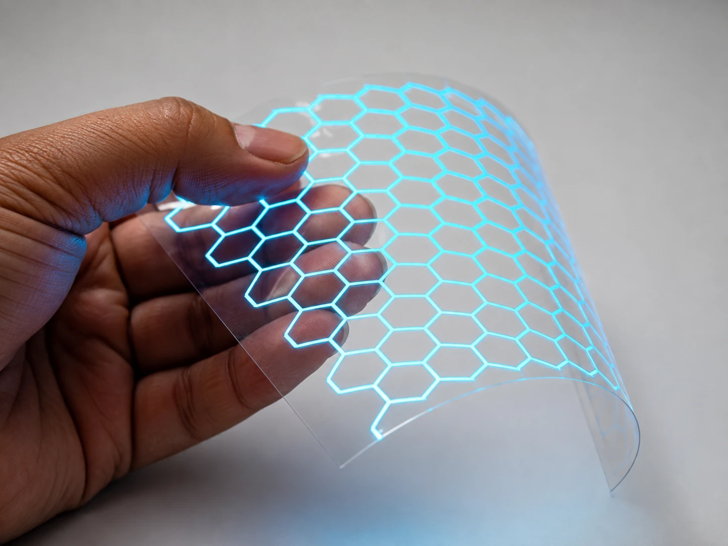 A hand bending a clear film printed with a glowing hexagon pattern